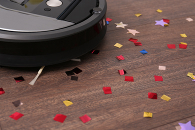 Photo of Modern robotic vacuum cleaner removing confetti from wooden floor, closeup. Space for text