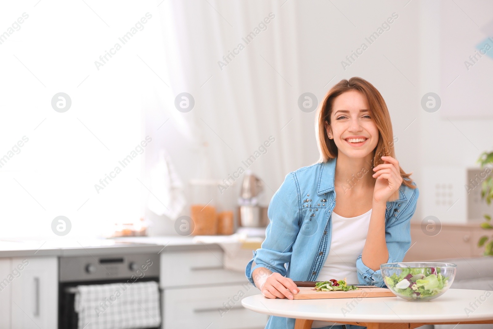 Photo of Happy young woman preparing salad in kitchen, space for text. Healthy diet