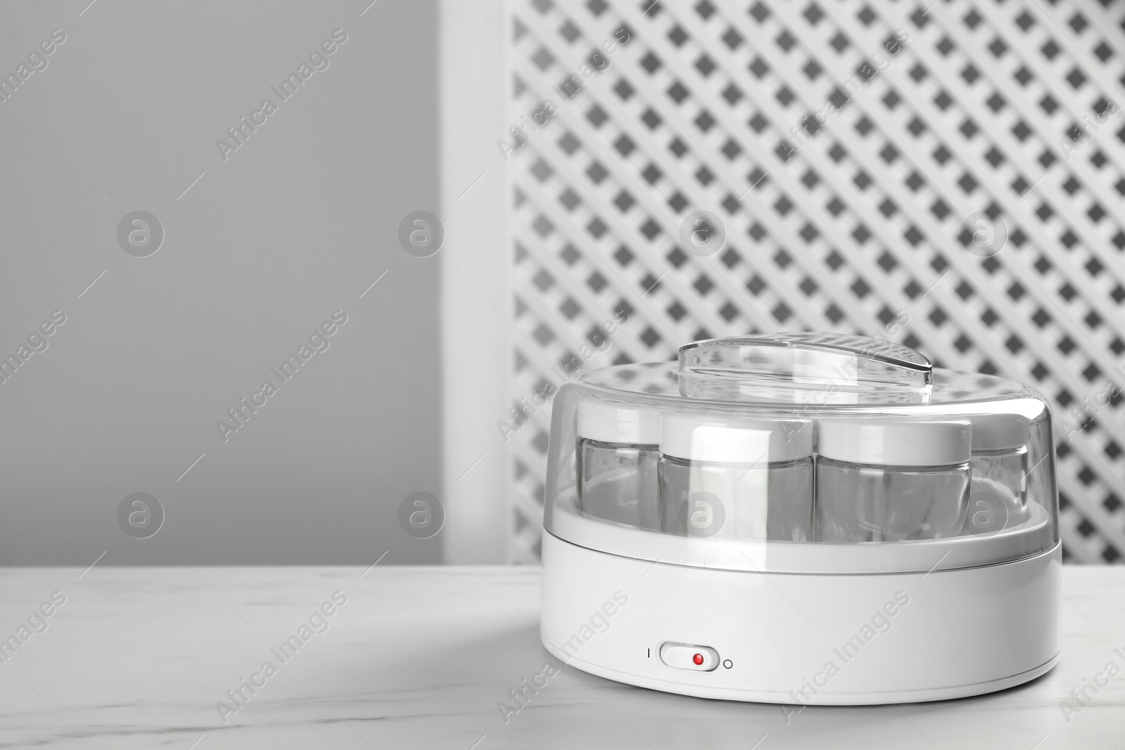 Photo of Modern yogurt maker with empty jars on white table indoors. Space for text