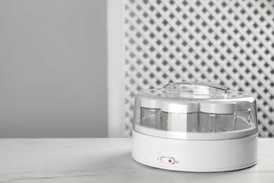 Photo of Modern yogurt maker with empty jars on white table indoors. Space for text