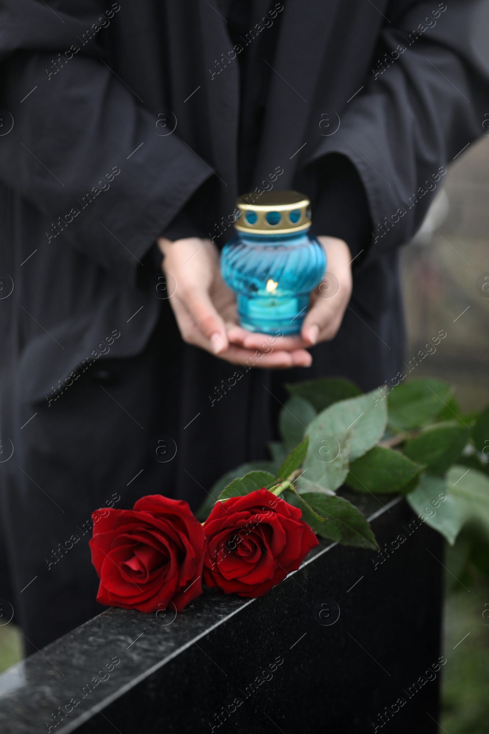 Photo of Woman with candle outdoors, focus on red roses. Funeral ceremony