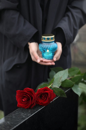 Photo of Woman with candle outdoors, focus on red roses. Funeral ceremony