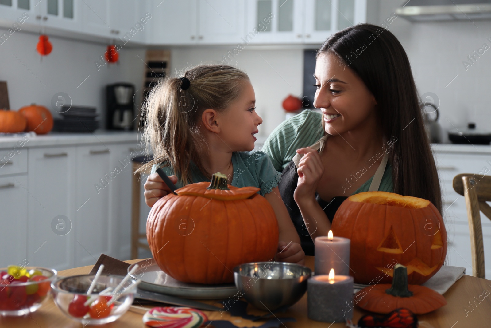 Photo of Mother and daughter making pumpkin jack o'lantern at table in kitchen. Halloween celebration