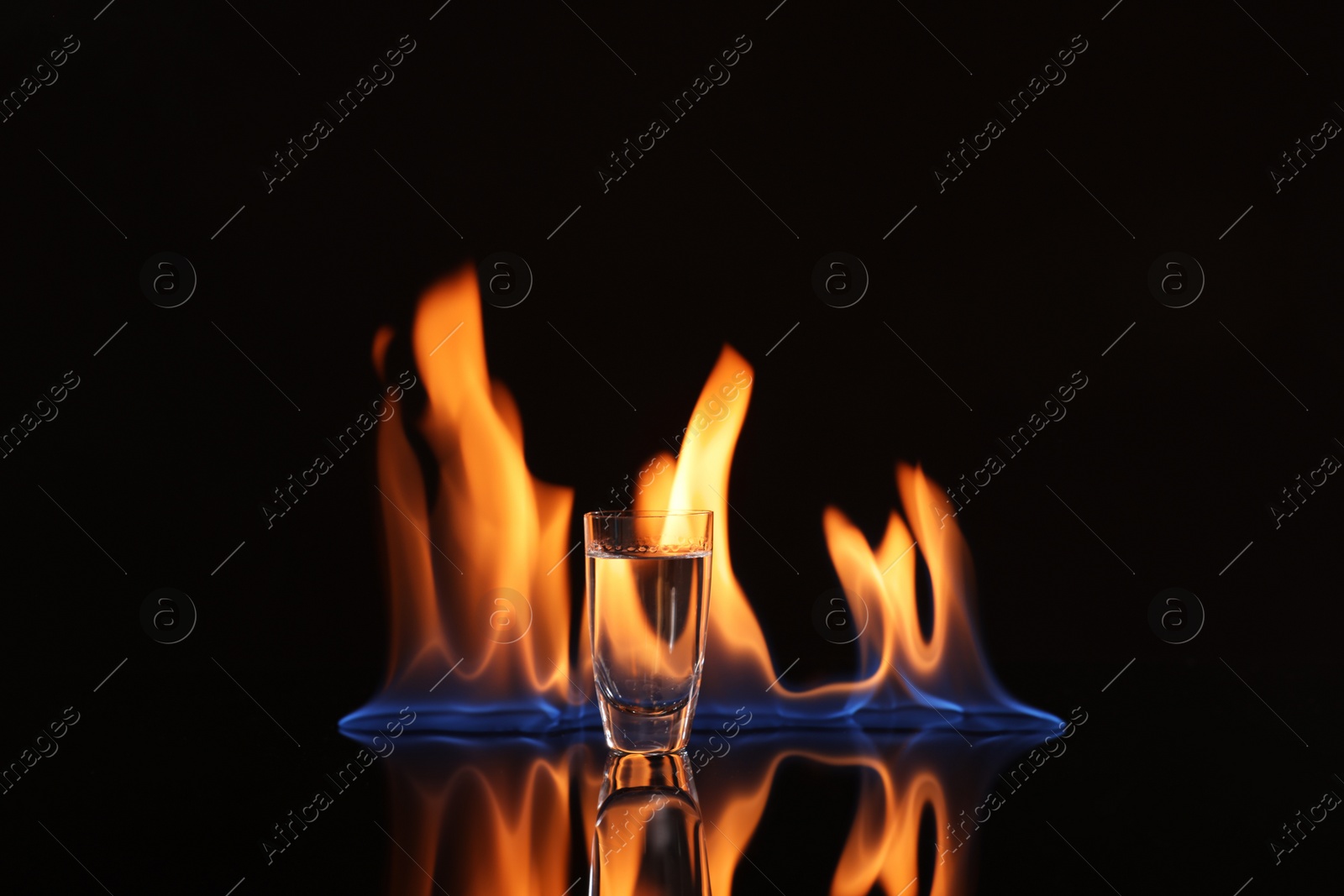 Photo of Vodka in shot glass and flame on black background