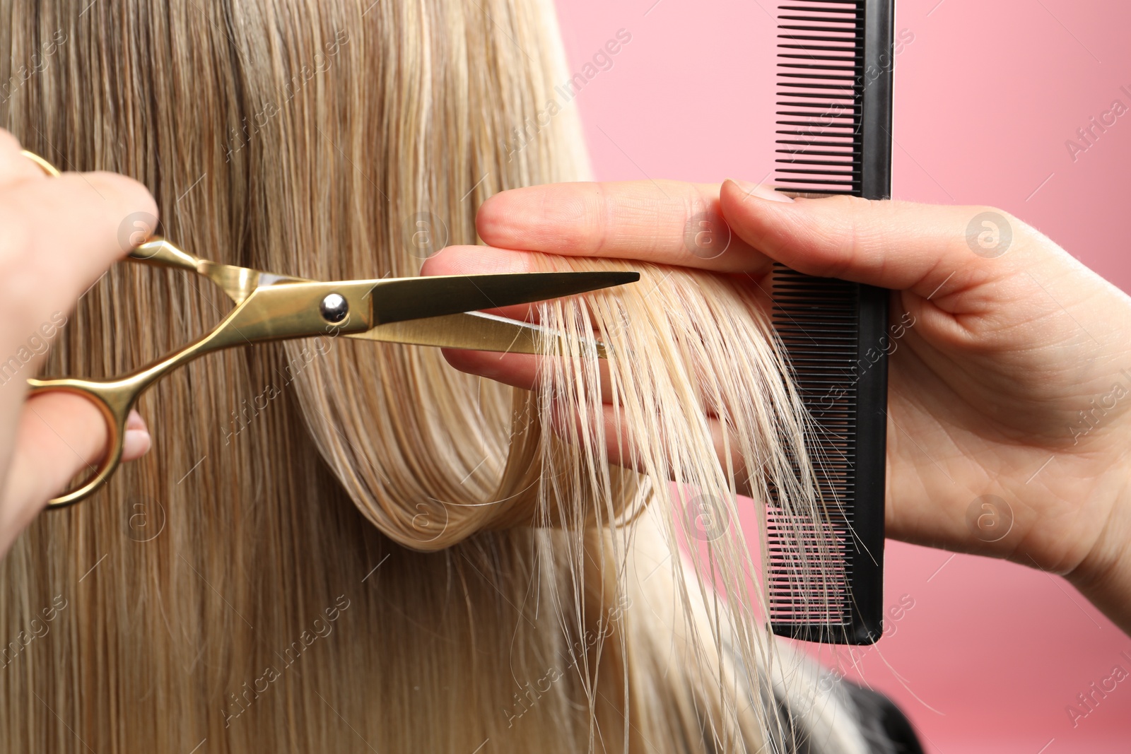 Photo of Hairdresser cutting client's hair with scissors on pink background, closeup