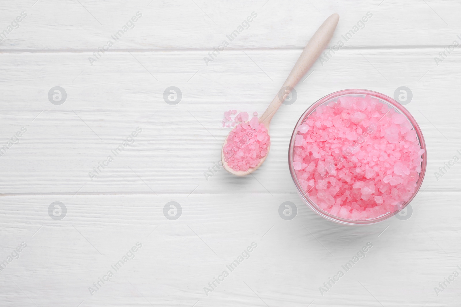 Photo of Bowl and spoon with pink sea salt on white wooden table, flat lay. Space for text