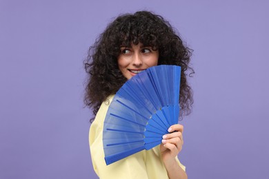 Happy woman holding hand fan on purple background