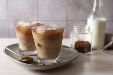 Photo of Refreshing iced coffee with milk in glasses, ingredients and spoon on light table, closeup