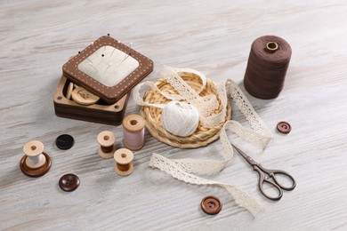 Photo of Color threads and different sewing accessories on white wooden table