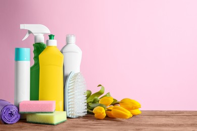 Spring cleaning. Detergents, tools and flowers on wooden table against pink background. Space for text