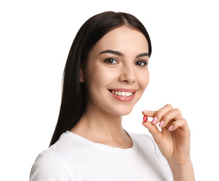 Young woman with vitamin capsule on white background