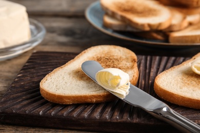 Toasted bread and knife with butter on wooden board