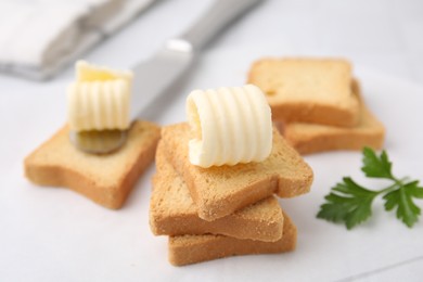 Photo of Tasty butter curls, knife and pieces of dry bread on white table, closeup