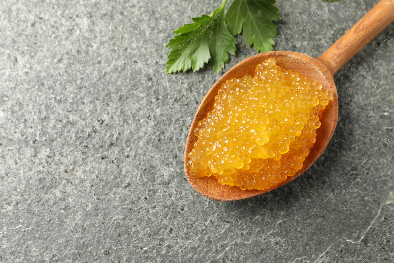 Photo of Fresh pike caviar in spoon and parsley on grey table, top view. Space for text