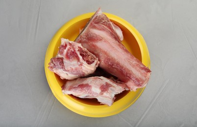 Feeding bowl with raw chopped meaty bones on grey table, top view. Natural animal food