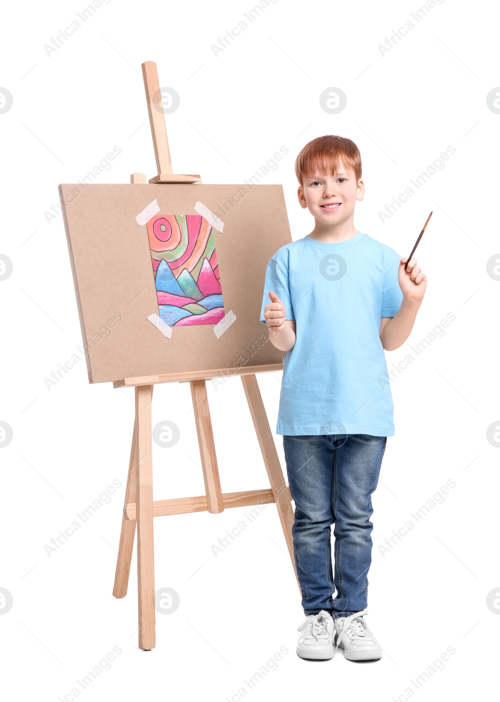 Photo of Little boy with brush near easel with canvas showing thumbs up against white background. Creative hobby