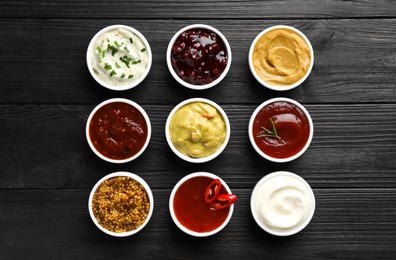 Photo of Different tasty sauces in bowls on black wooden table, flat lay