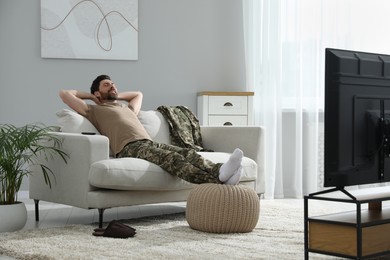 Soldier napping on soft sofa near TV in living room. Military service