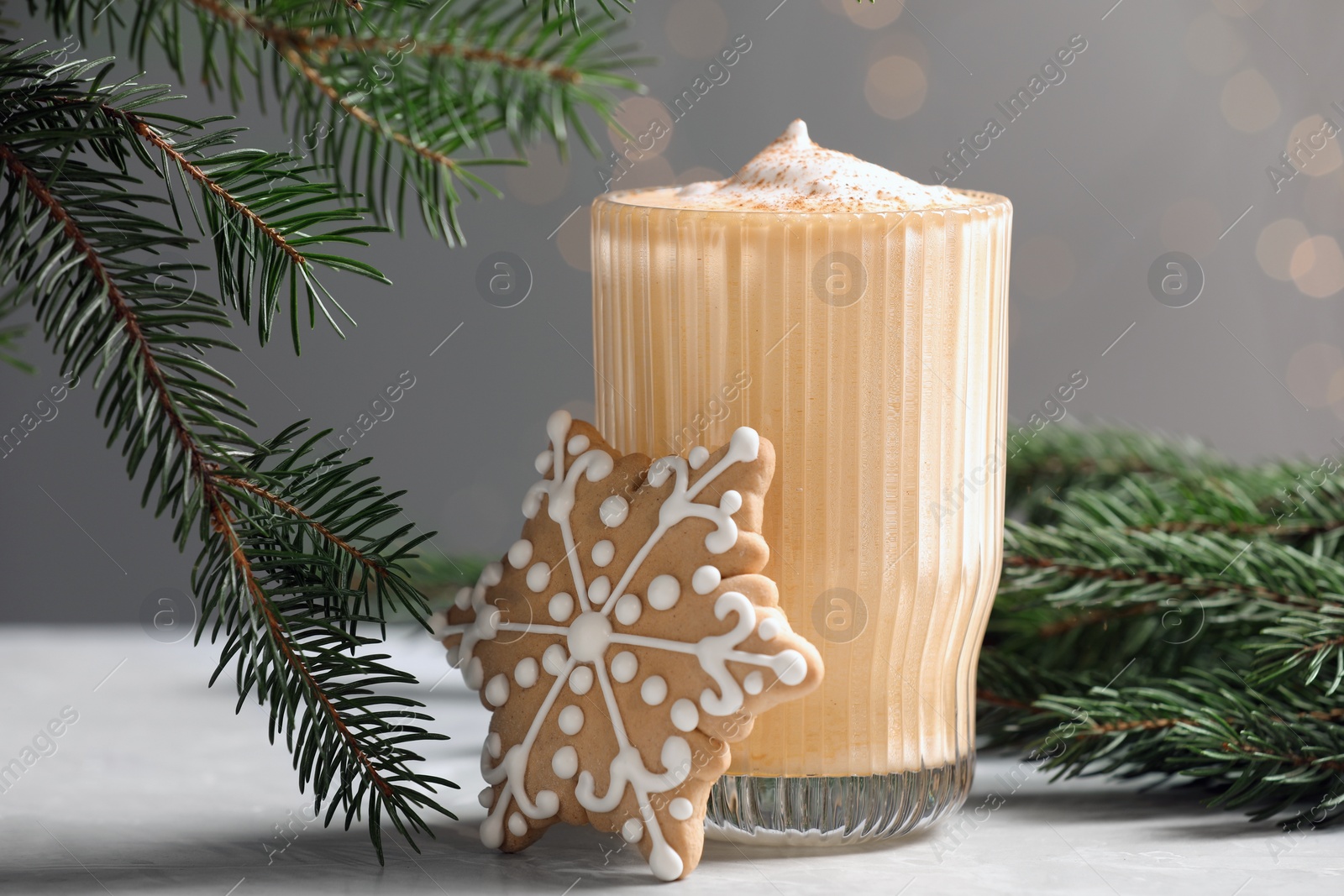 Photo of Tasty eggnog, cookie and fir branches on grey textured table