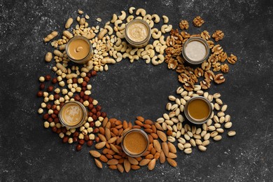 Frame of tasty nut butters in jars and raw nuts on dark gray table, flat lay. Space for text