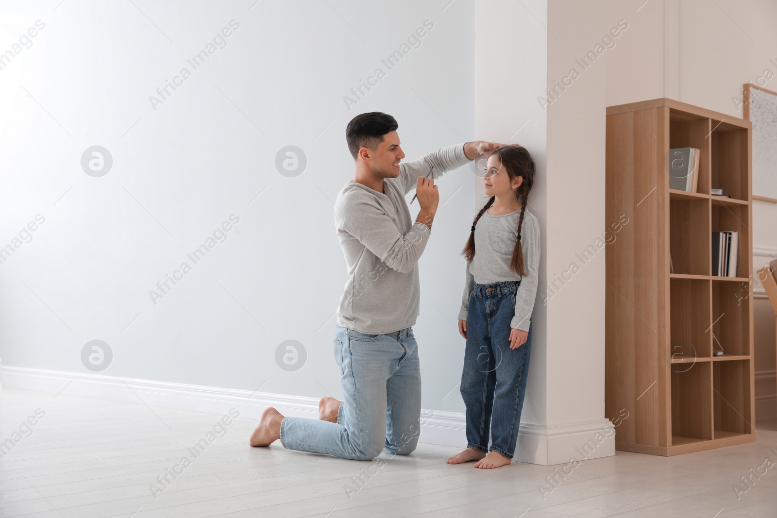 Photo of Father measuring height of his daughter near wall at home