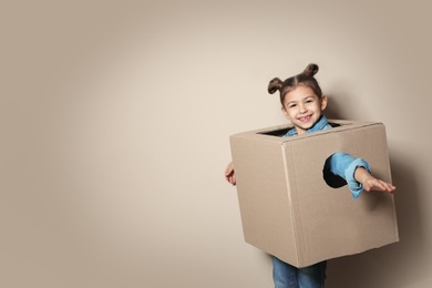 Photo of Cute little girl playing with cardboard box on color background. Space for text
