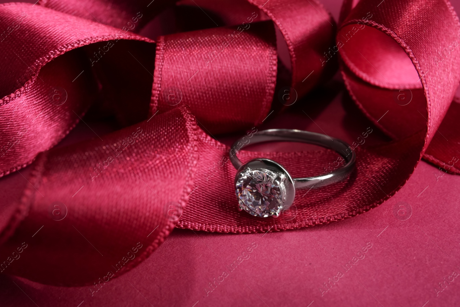 Photo of Beautiful luxury engagement ring with gemstone and ribbons on marsala background, closeup