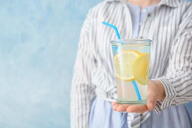 Young woman holding glass with lemon cocktail against color background