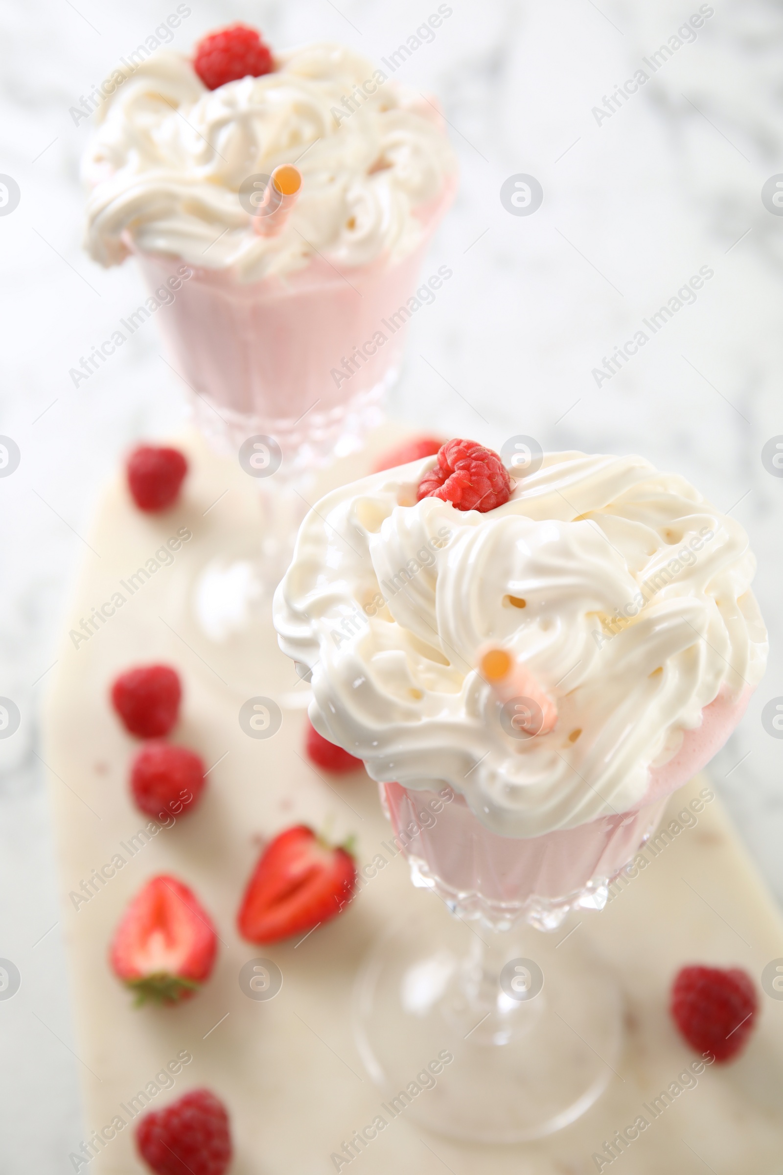 Photo of Tasty milk shake with whipped cream and fresh berries on light table, closeup