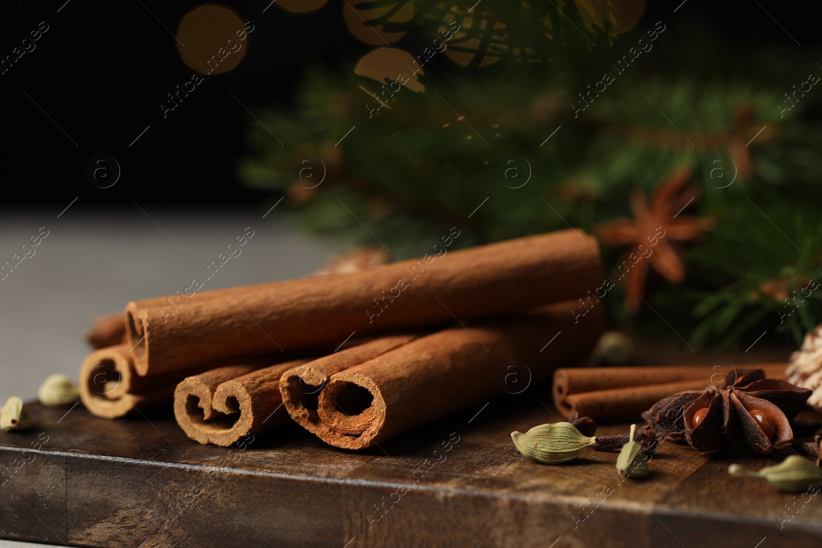 Photo of Different aromatic spices on wooden board against black background, closeup