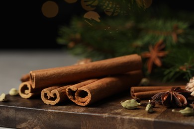 Photo of Different aromatic spices on wooden board against black background, closeup