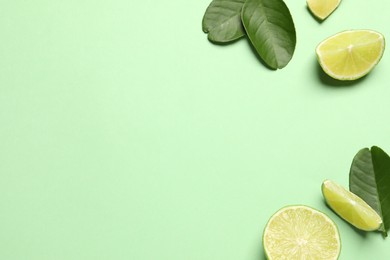 Photo of Cut fresh ripe limes with leaves on light green background, flat lay