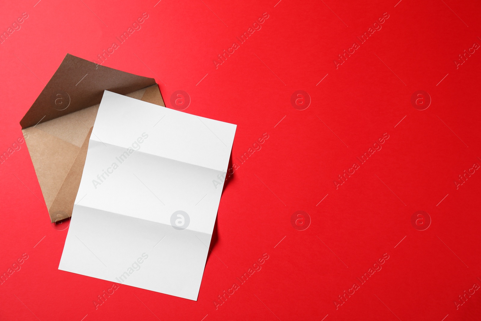 Photo of Blank sheet of paper and letter envelope on red background, top view. Space for text