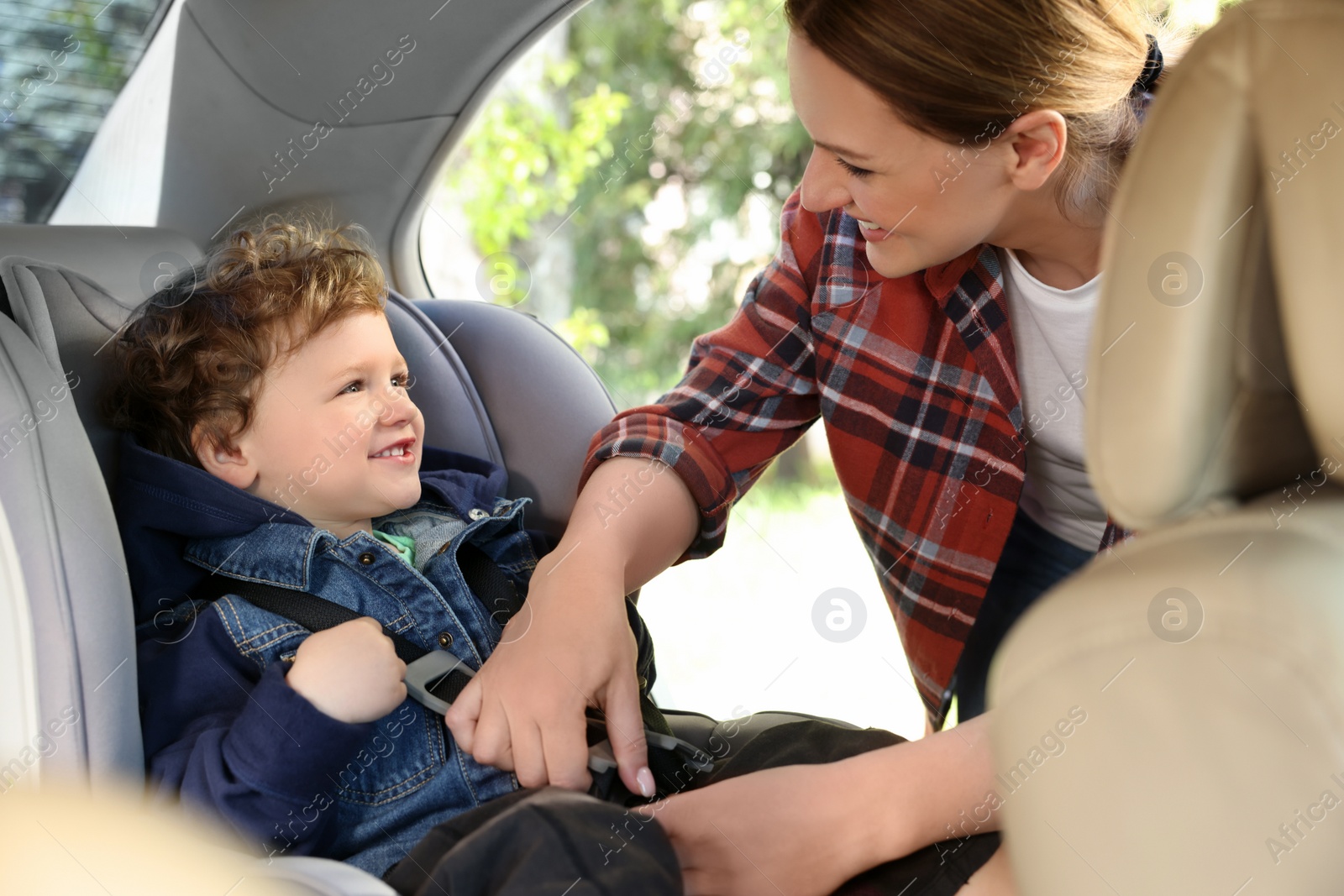 Photo of Mother fastening her son in child safety seat inside car