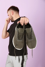 Photo of Young man feeling bad smell from shoes on color background. Air freshener