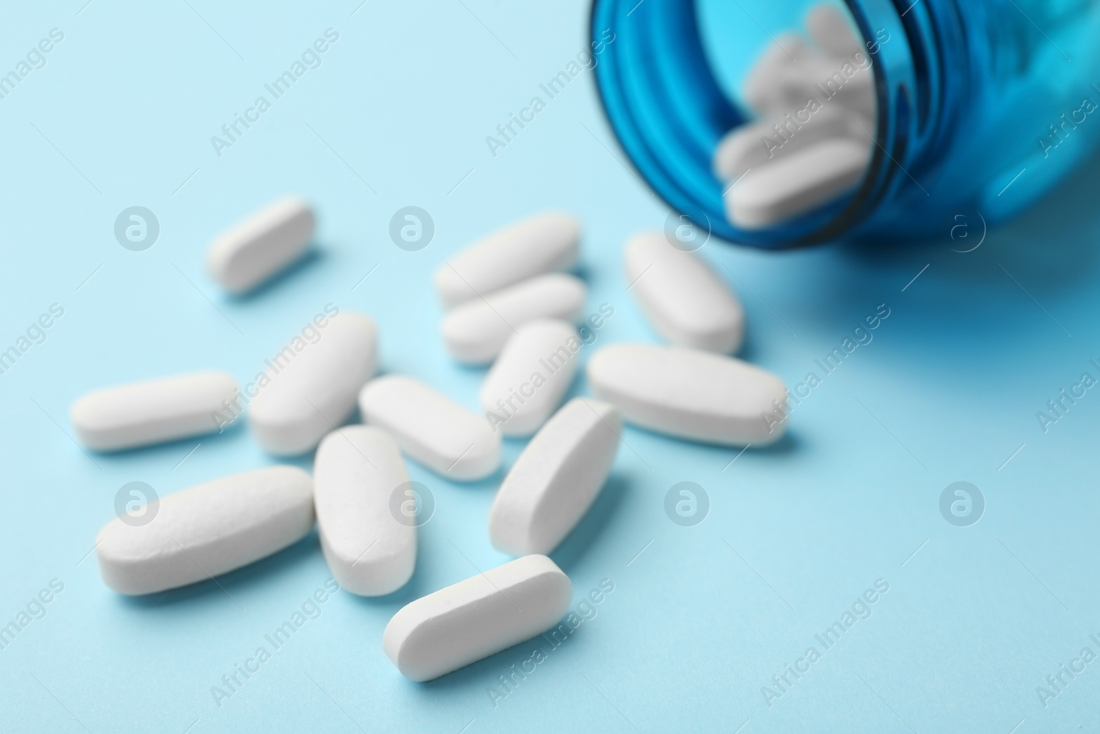 Photo of Vitamin pills and bottle on light blue background, closeup