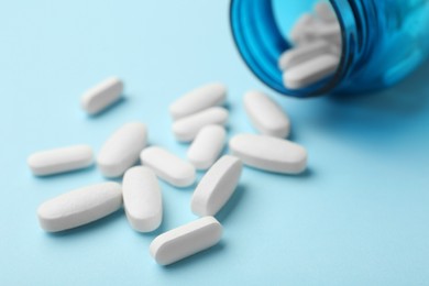 Vitamin pills and bottle on light blue background, closeup