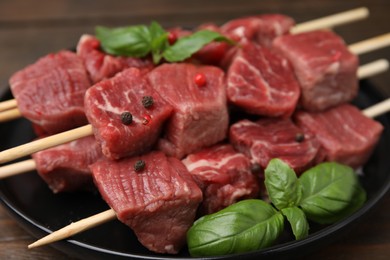 Photo of Wooden skewers with cut fresh beef meat, basil leaves and spices on table, closeup