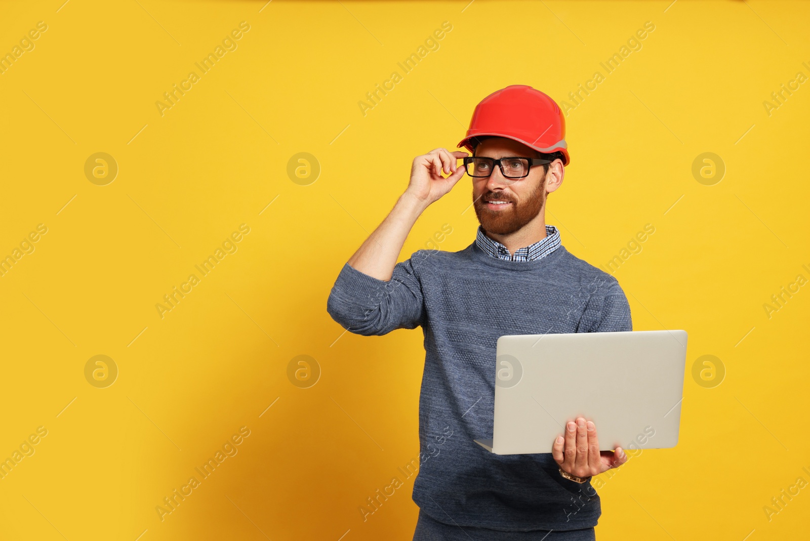 Photo of Professional engineer in hard hat with laptop on yellow background, space for text