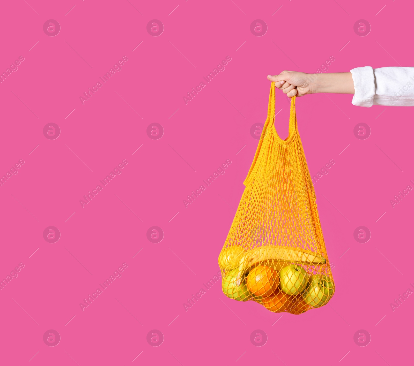 Photo of Woman holding net bag with fruits on pink background, closeup