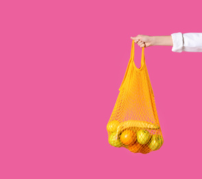 Photo of Woman holding net bag with fruits on pink background, closeup