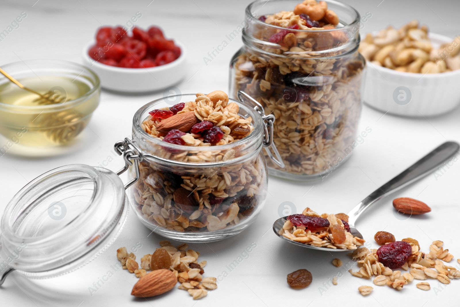 Photo of Jars of tasty granola with nuts and dry fruits on white marble table