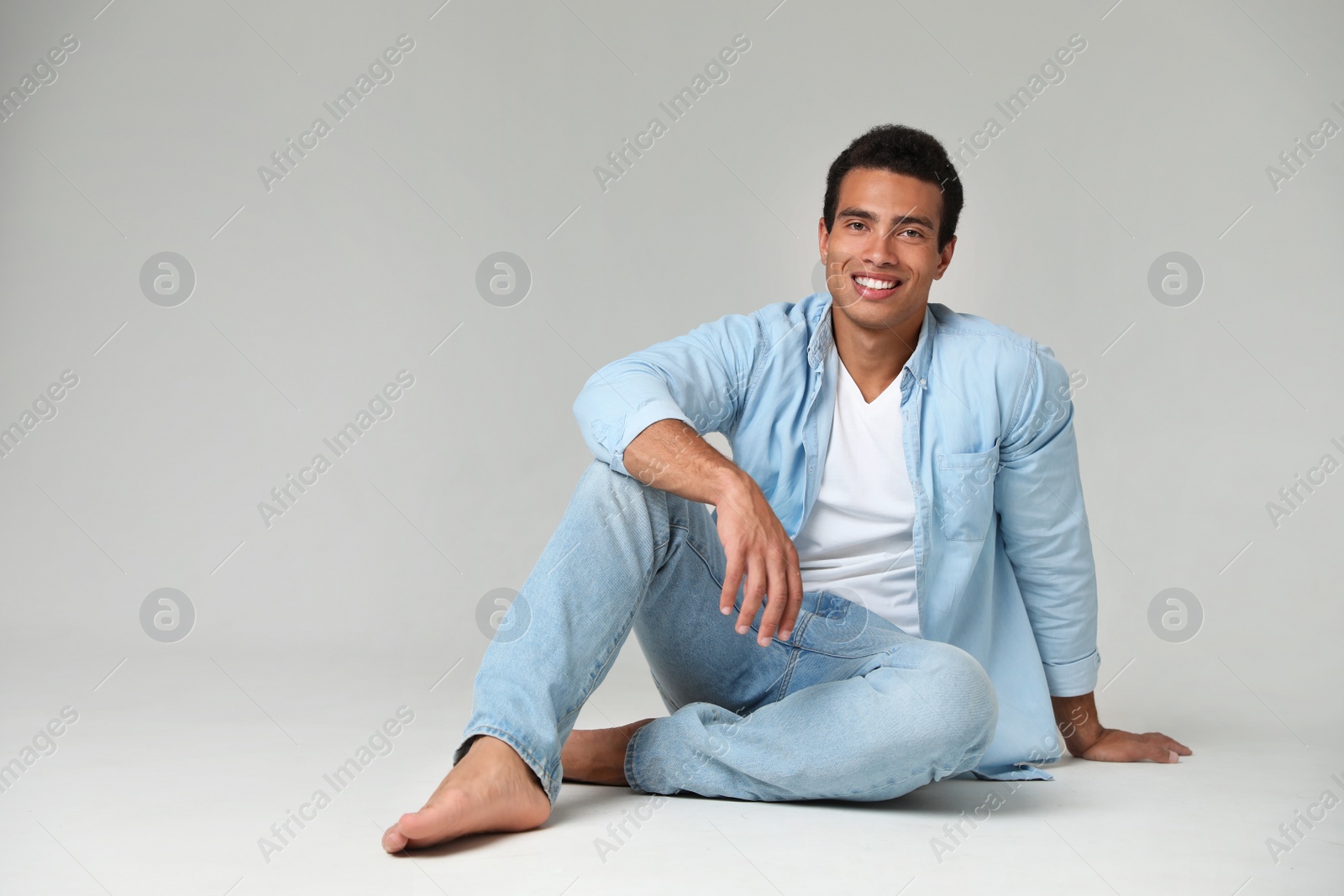 Photo of Handsome young African-American man sitting on light background. Space for text