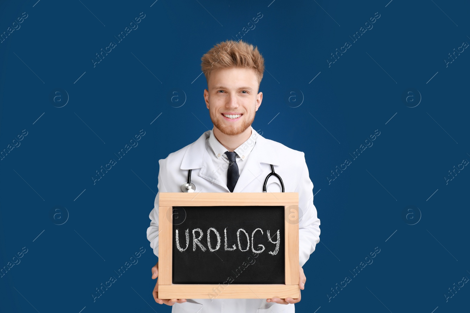 Photo of Male doctor holding small blackboard with word UROLOGY on blue background