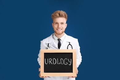 Male doctor holding small blackboard with word UROLOGY on blue background