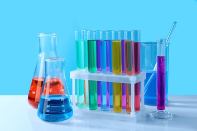Different laboratory glassware with colorful liquids on white table against light blue background