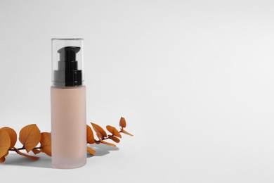 Bottle of skin foundation and decorative branch on white background, space for text. Makeup product