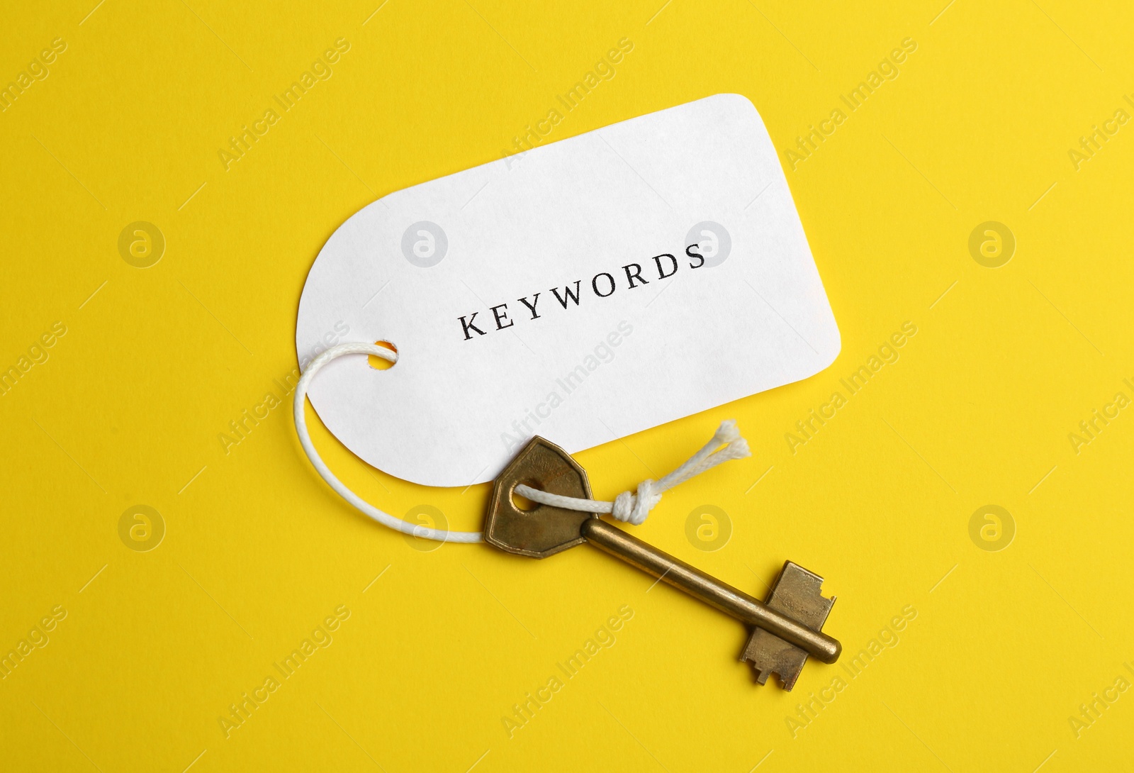 Photo of Metal key and tag wIth word KEYWORDS on yellow background, top view