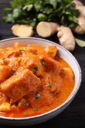 Photo of Bowl of delicious chicken curry on black wooden table, closeup