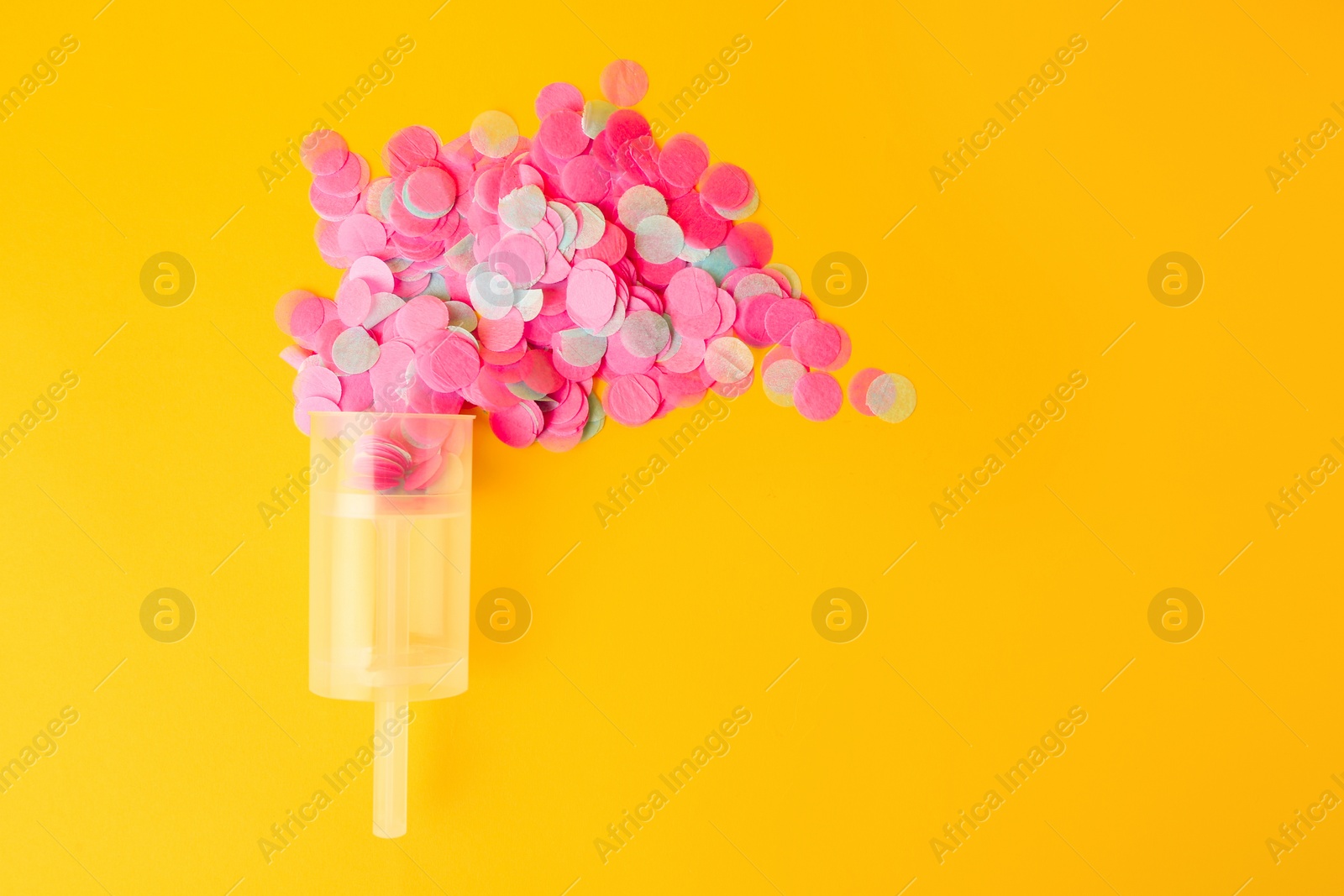 Photo of Colorful confetti bursting out of transparent party popper on yellow background, flat lay. Space for text